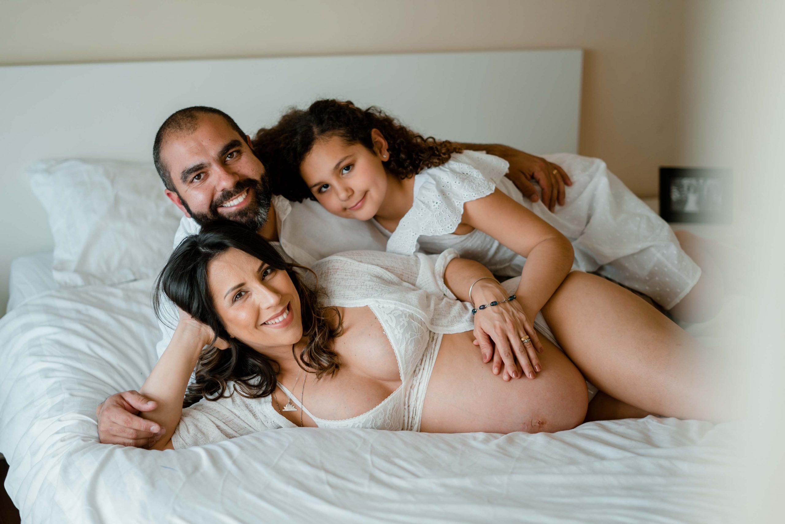 maternity films and photos: Family lying down on bed, pregnant mum at front, daddy behind and 8 years girl on top of them