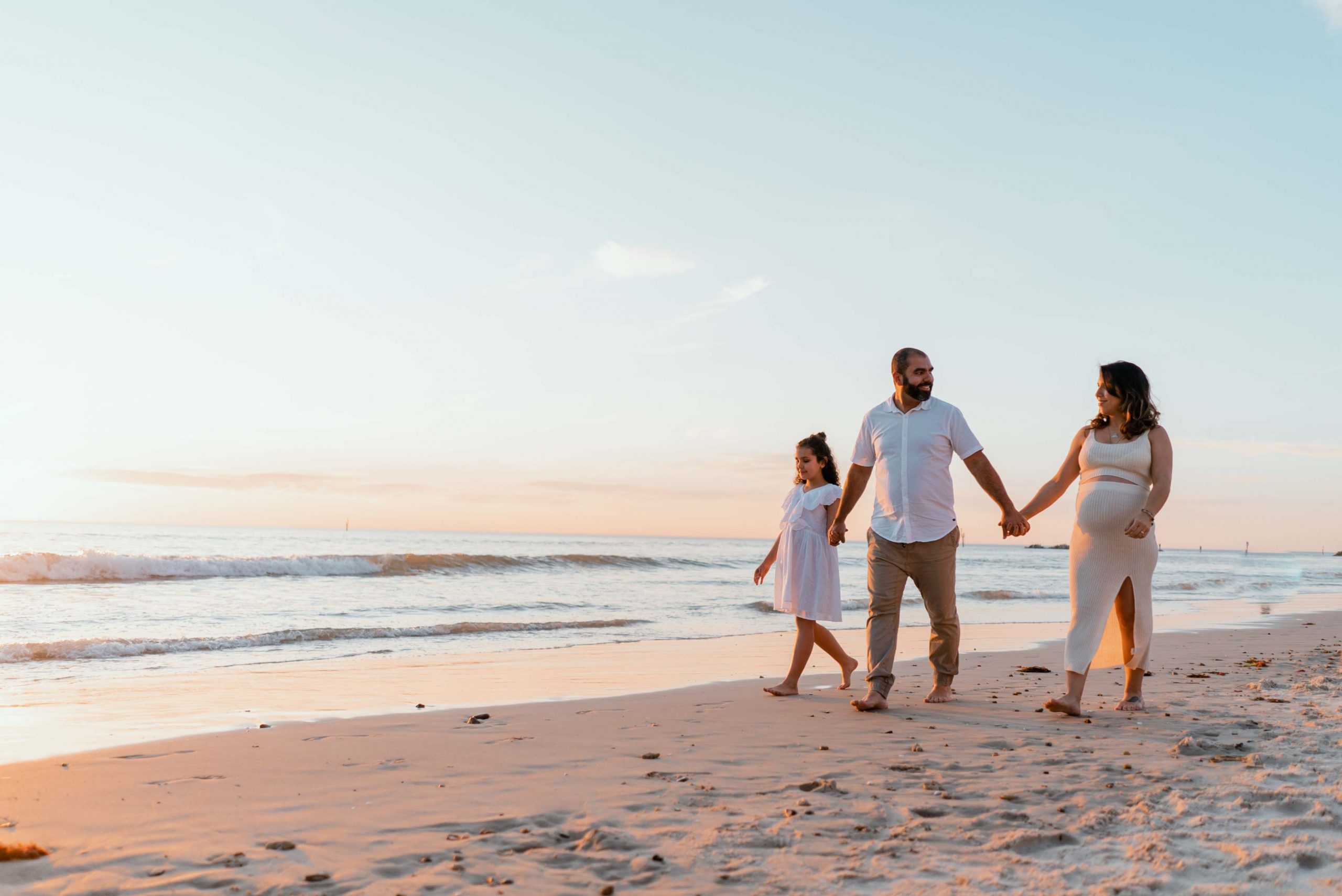 maternity films and photos: sunset time with family walking in the beach looking at each other and expecting their second child