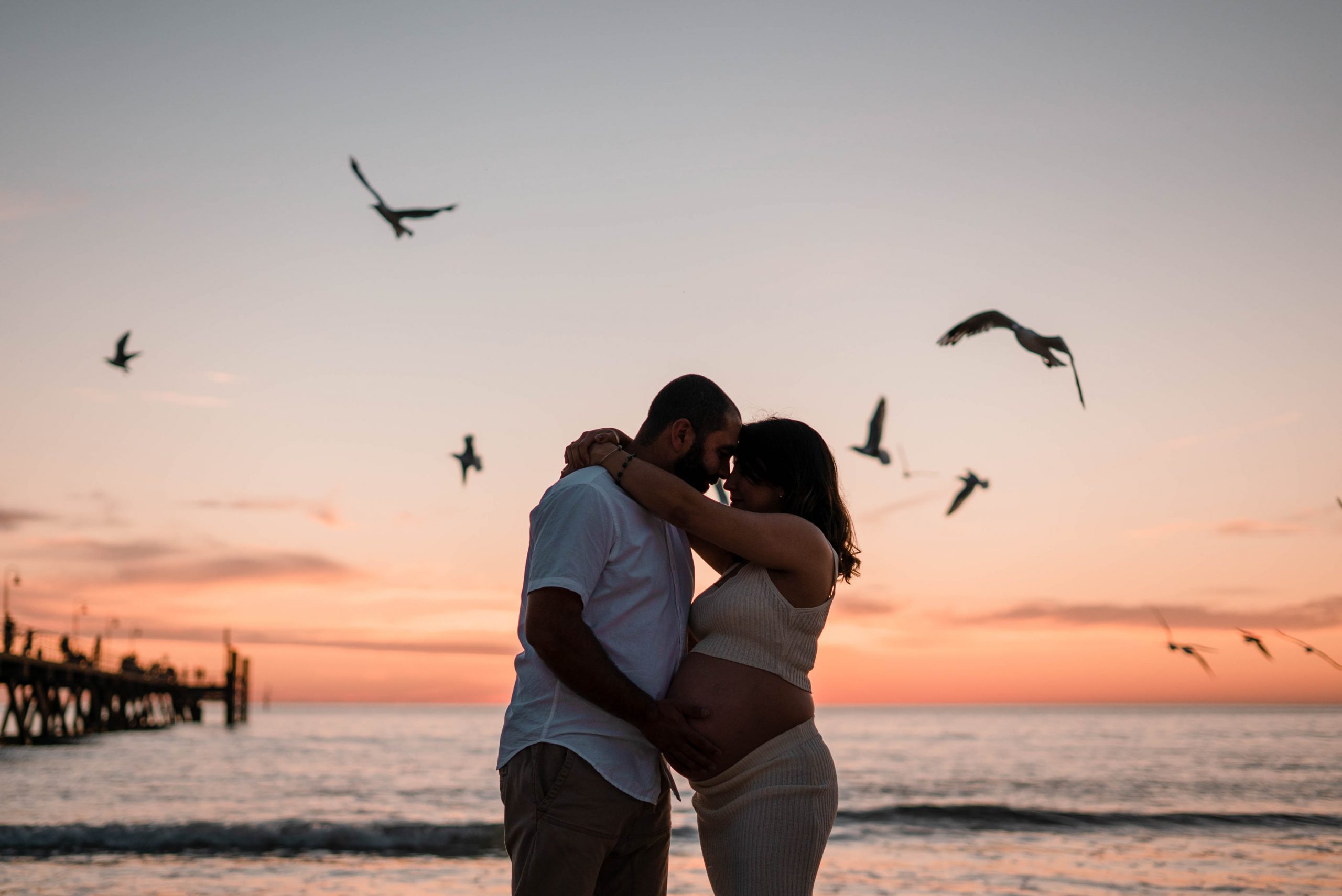 maternity films and photos: sunset full of birds flying in the background with a pregnant couple looking at each other