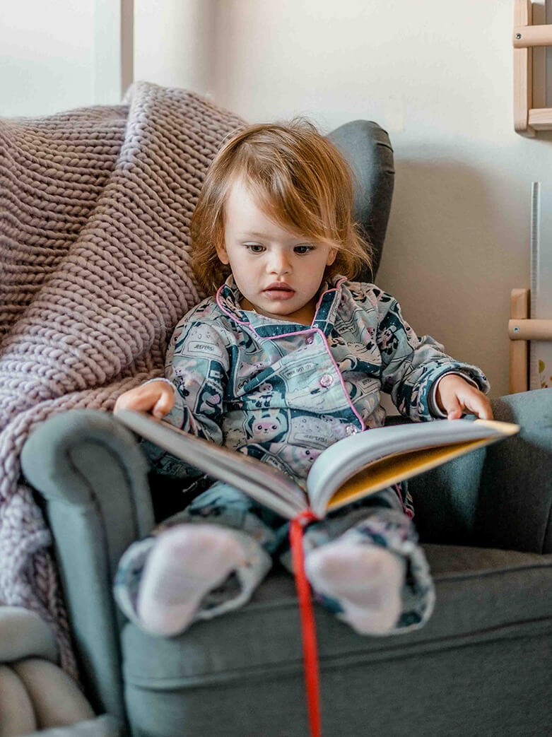 family films and photos: 2 year girl wearing pyjamas sitting in her small couch and reading a book