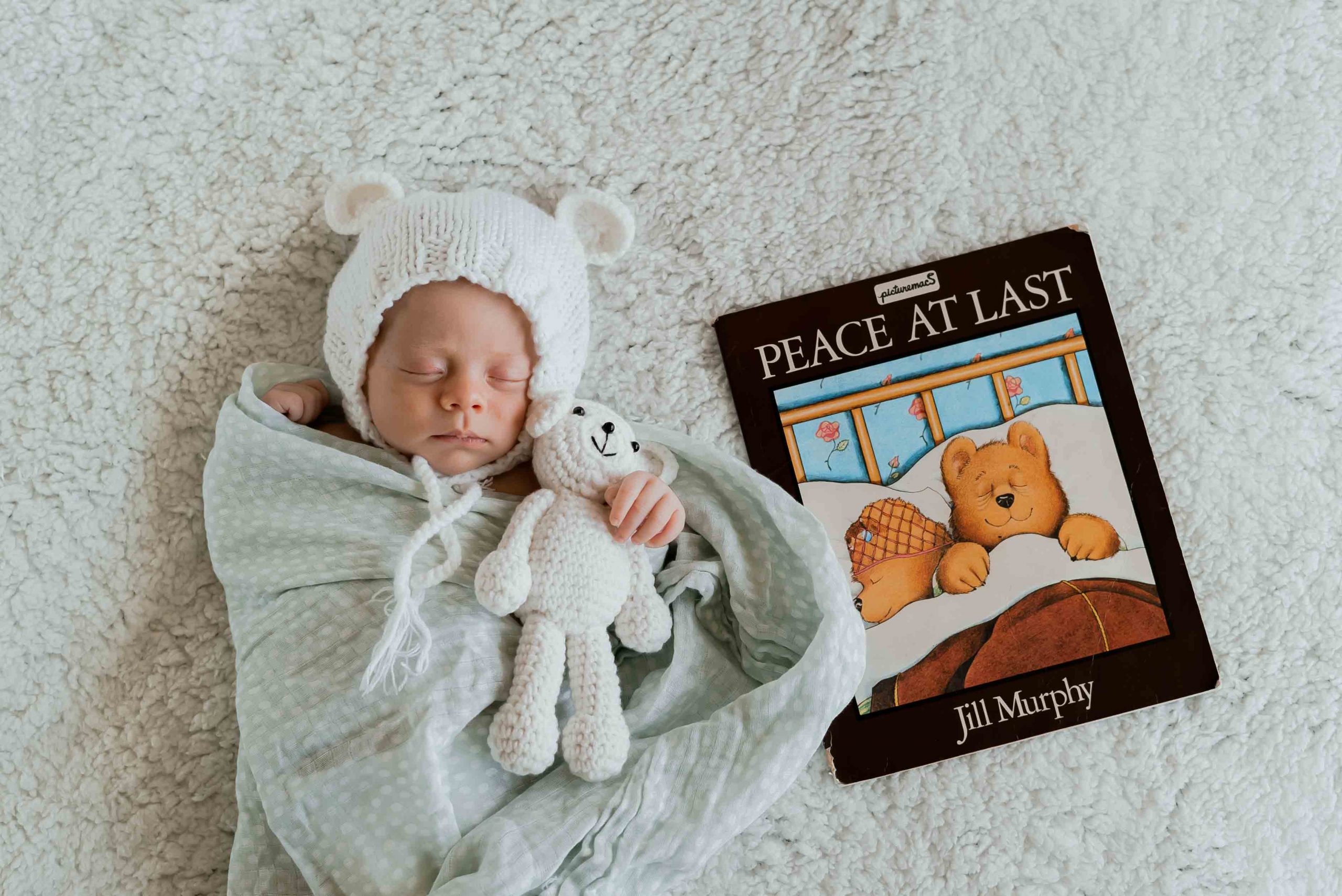 newborn films and photos: baby sleeping with a puppet in his hands, next to him a kid's book
