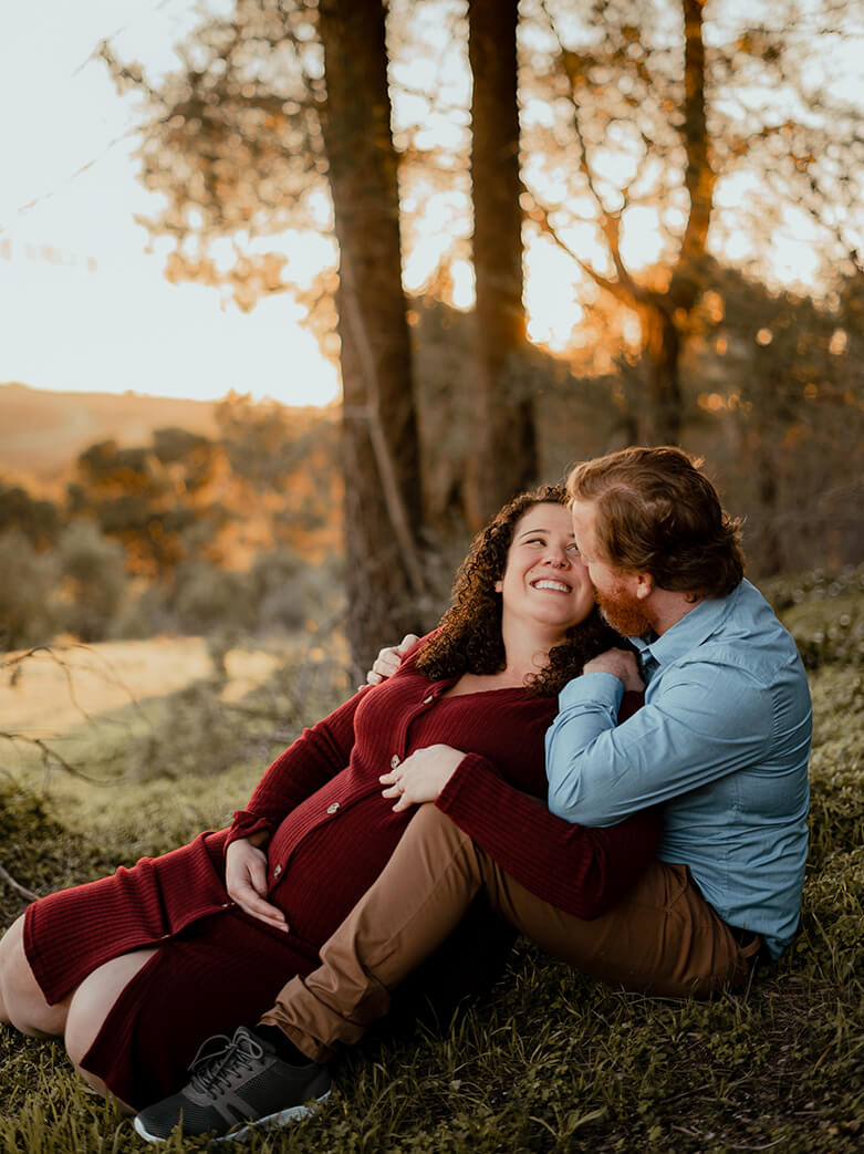maternity films and photos: happy couple expecting a baby, siting on the grass at the sunset